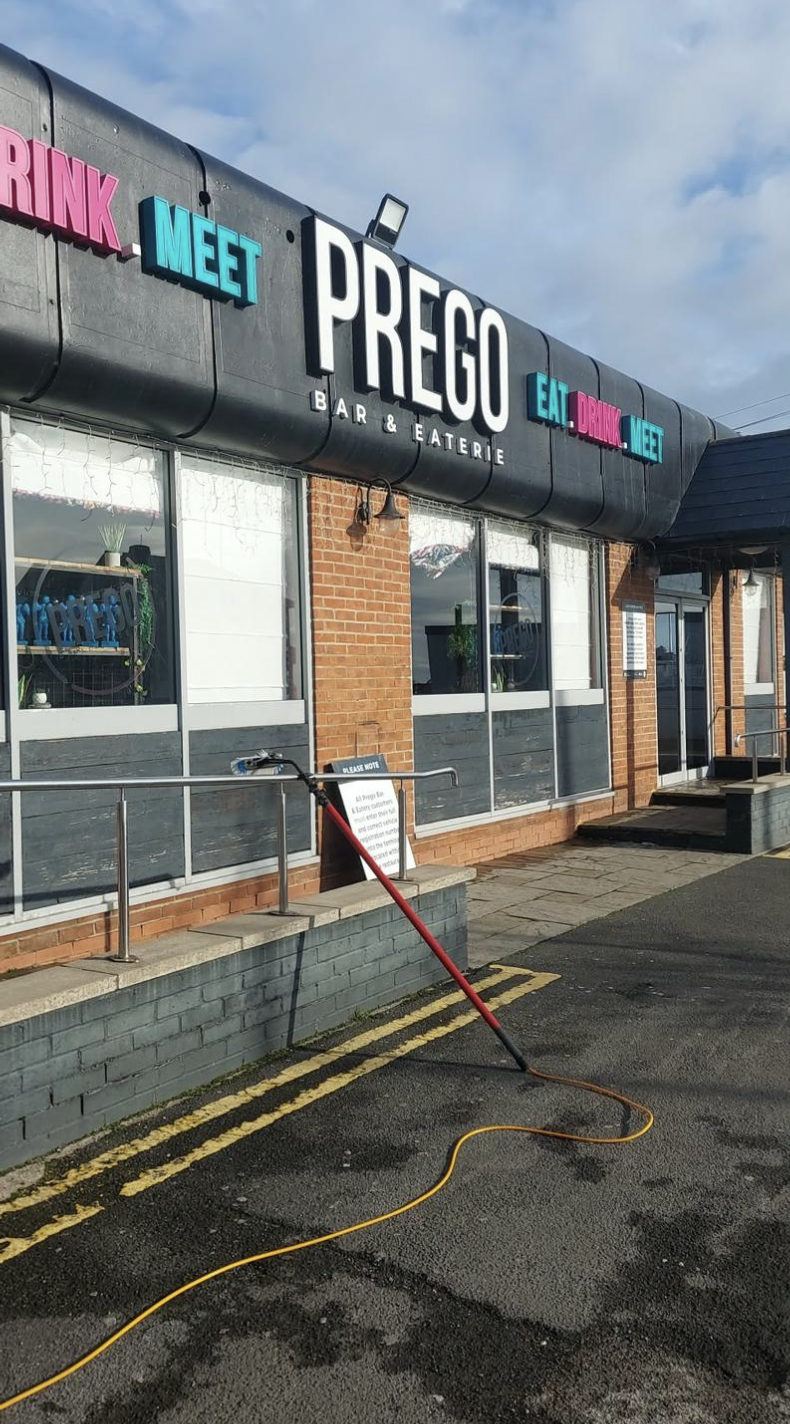Professional window cleaner working on a modern glass building with blue sky reflection
